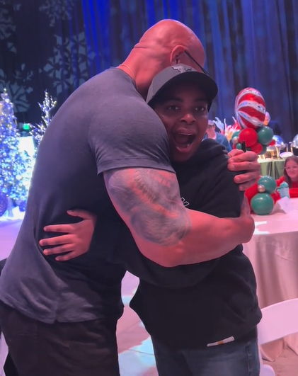 A young boy named Trenton hugs Dwayne "The Rock" Johnson with his mouth agape from shock.