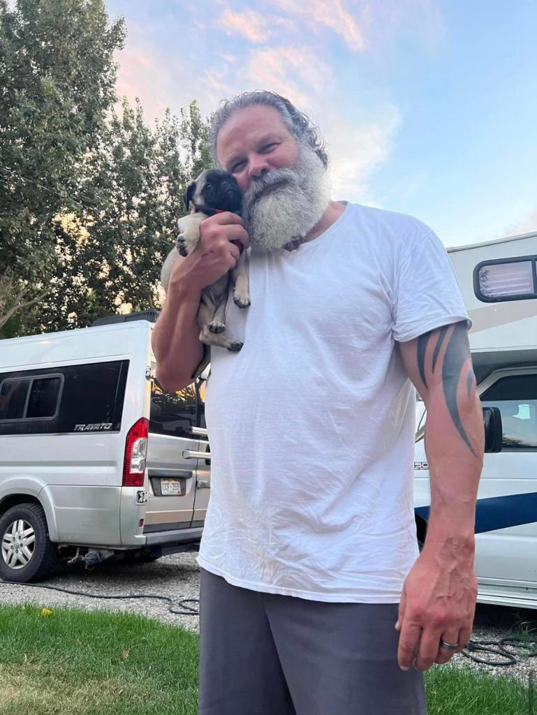 A man with a grey beard smiling while holding a puppy.
