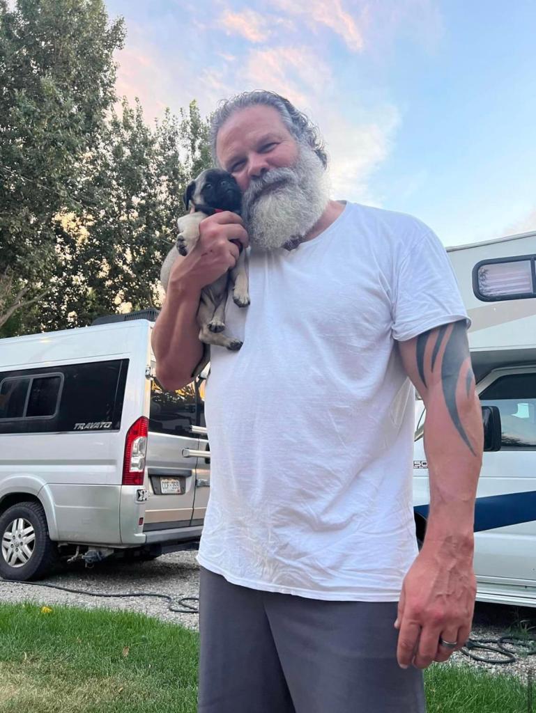 A man with a grey beard smiling while holding a puppy. 