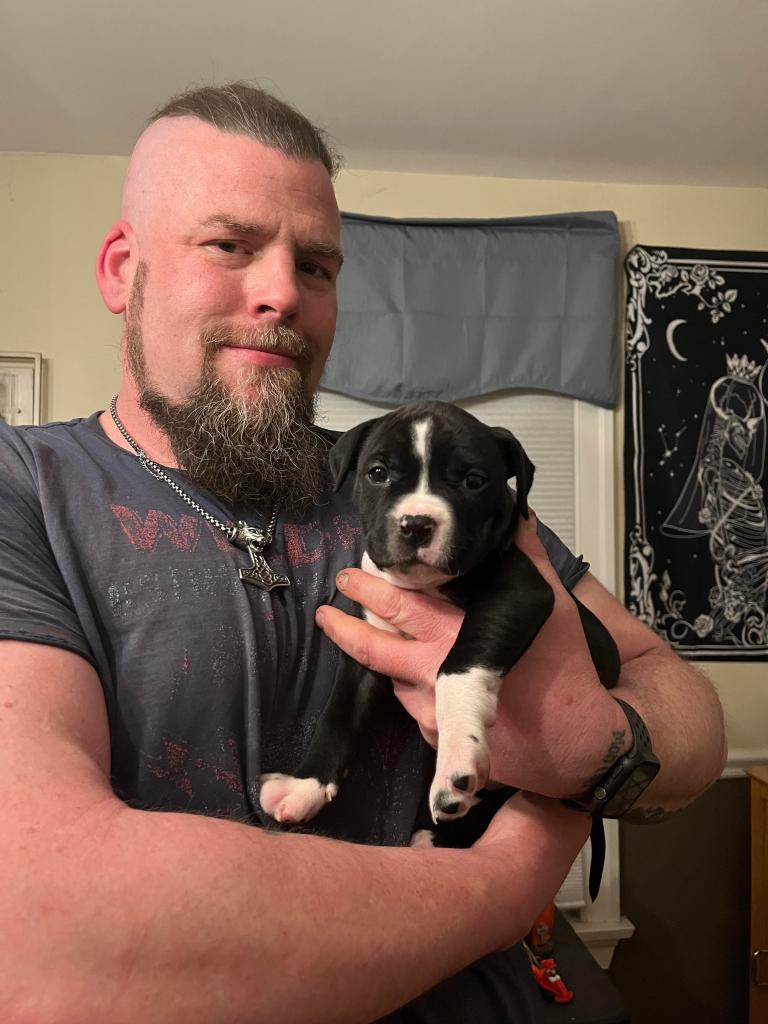 A big, tough-looking guy holding his tiny pet dog. 