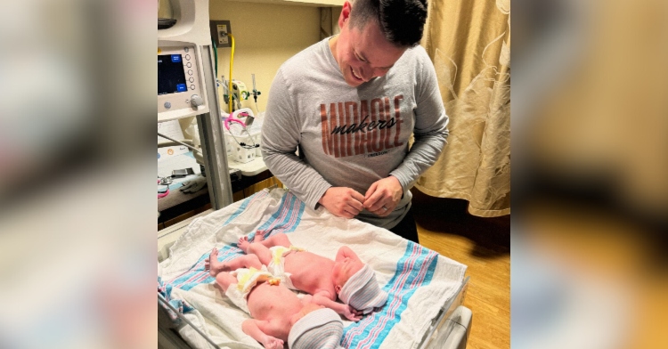 Billy Humphrey smiles wide as he looks down at his twins born in different years. They are laying on their backs in the hospital.