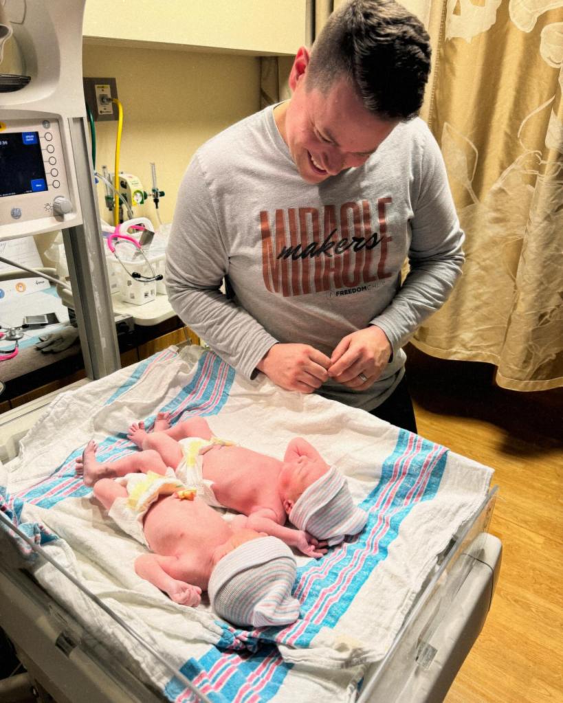 Billy Humphrey smiles wide as he looks down at his twins born in different years. They are laying on their backs in the hospital.