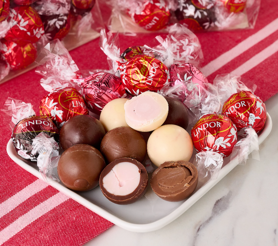 View of Lindt Lindor chocolates on a small, square plate. Some are still in their container but others are unwrapped and others are unwrapped and cut in half.