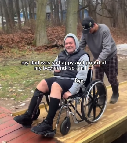 A young man pushes his girlfriend's dad up a wheelchair ramp. 