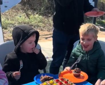 One little boy eats cake at a birthday party while another smiles at his cupcake.