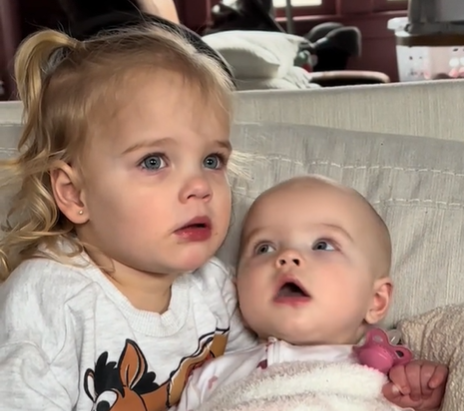 A little girl holds her baby sister while watching "Ms. Rachel."