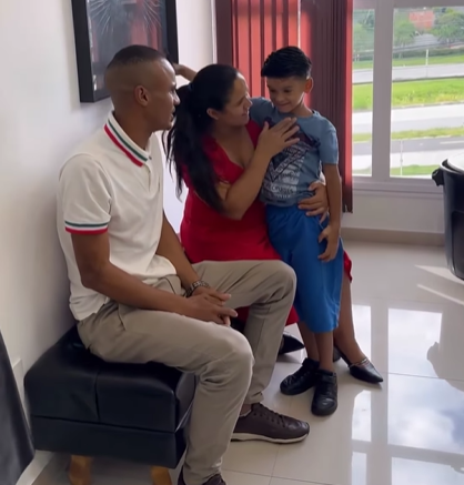 A little boy smiles as his mom holds him close. Dad sits next to mom, watching them.