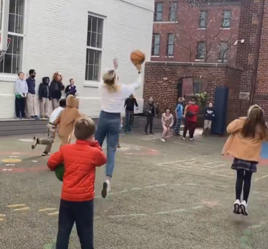 A teacher plays basketball with her students. 