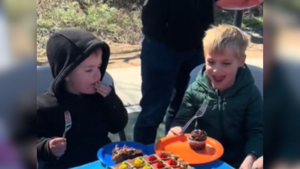 One little boy eats cake at a birthday party while another smiles at his cupcake.