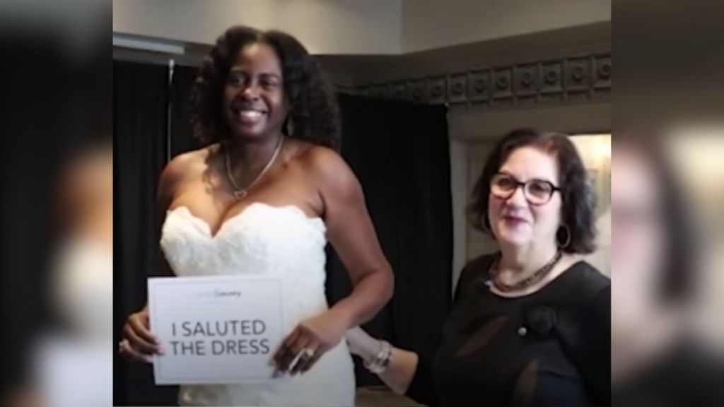 A woman stands next to a veteran in a wedding gown holding a sign that says "I saluted the dress.