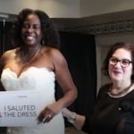 A woman stands next to a veteran in a wedding gown holding a sign that says "I saluted the dress.