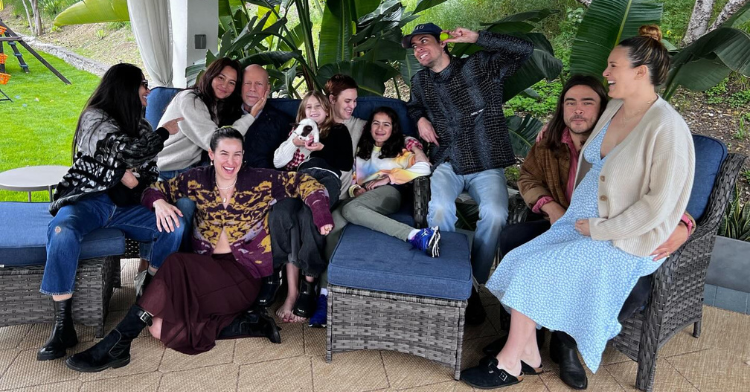 Bruce Willis smiles as he poses for a photo outside with his family, including his wife Emma and his ex-wife Demi Moore.