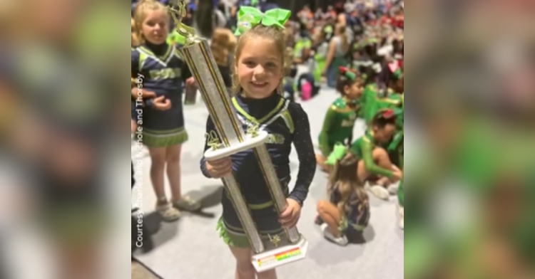 An 8-year-old girl smiles as she holds her first place trophy after she performs alone.