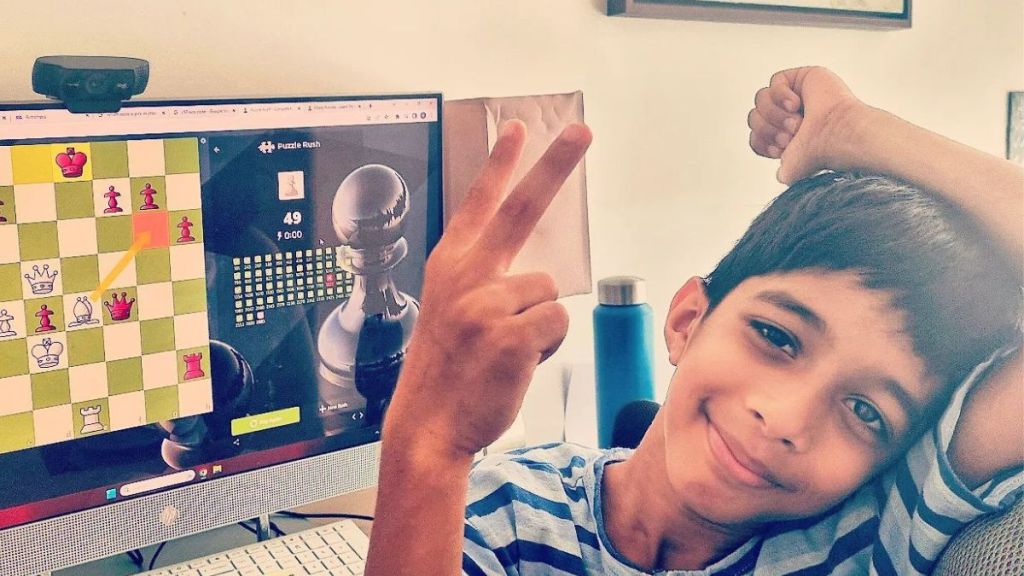 A young boy poses in front of a chess game on his computer.