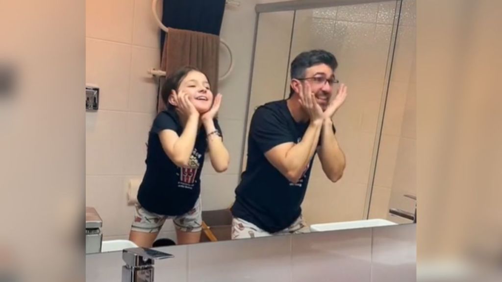 A dad and daughter doing a choreographed dance in the mirror.