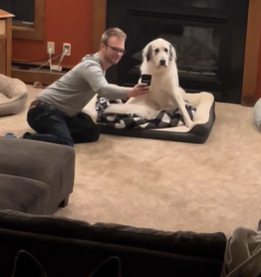 A man sits on the floor to take a selfie with a fluffy dog.