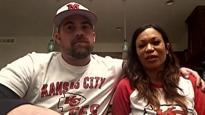 Trey and Casey Filter sit on a couch in their home. Trey has an arm around Casey. They're both wearing Kansas City Chiefs merch.