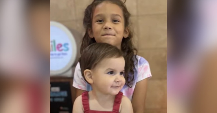 Charley smiles as she stands behind her sister, Autumn, who smiles while looking off in the distance.