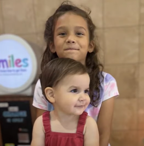 Charley smiles as she stands behind her sister, Autumn, who smiles while looking off in the distance.