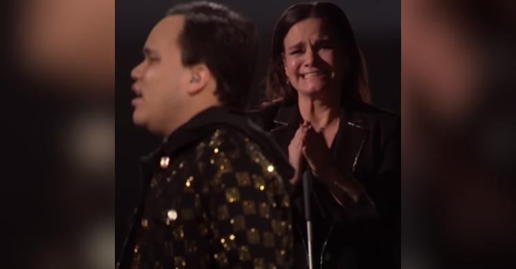 Side view of Kodi Lee on "AGT" as his mom, Tina Lee, approaches from off stage. She's clapping. She also smiles while holding back tears, though it's clear she's already cried.