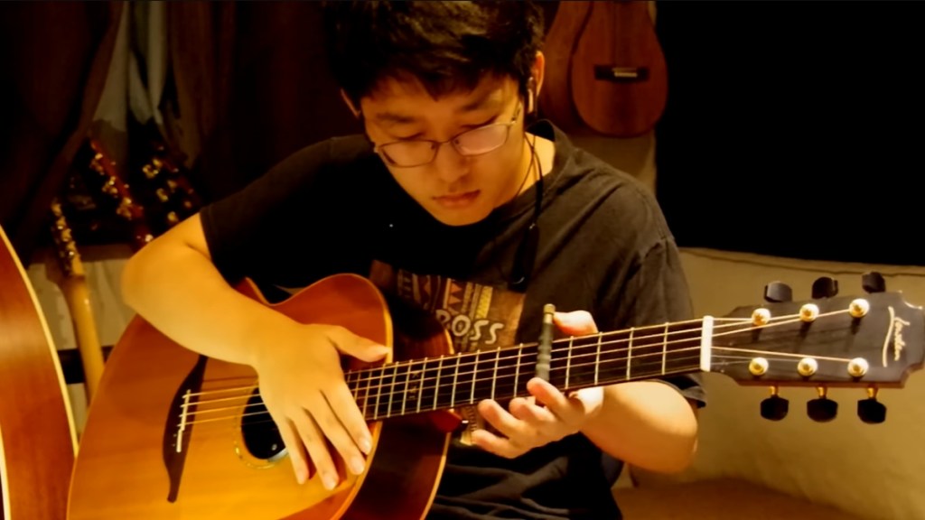 Kent Nishimura looks down as he plays "Man in the Mirror" on his acoustic guitar.