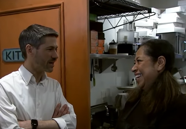 A man in a white shirt talks to a smiling woman with pigtails.