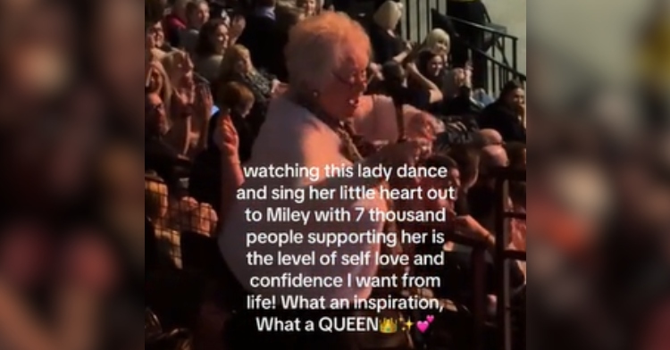 An elderly woman smiles as she interacts with the crowd and dances to "Flowers" at a Miley Cyrus concert. Text on the image reads: Watching this lady dance and sing her little heart out to Miley with 7,000 people supporting her is the level of self-love and confidence I want from life! What an inspiration, what a QUEEN.
