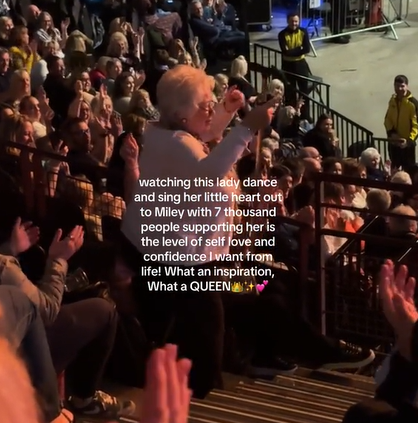An elderly woman points her index fingers in the air as she dances at a Miley Cyrus concert. Text on the image reads: Watching this lady dance and sing her little heart out to Miley with 7,000 people supporting her is the level of self-love and confidence I want from life! What an inspiration, what a QUEEN.