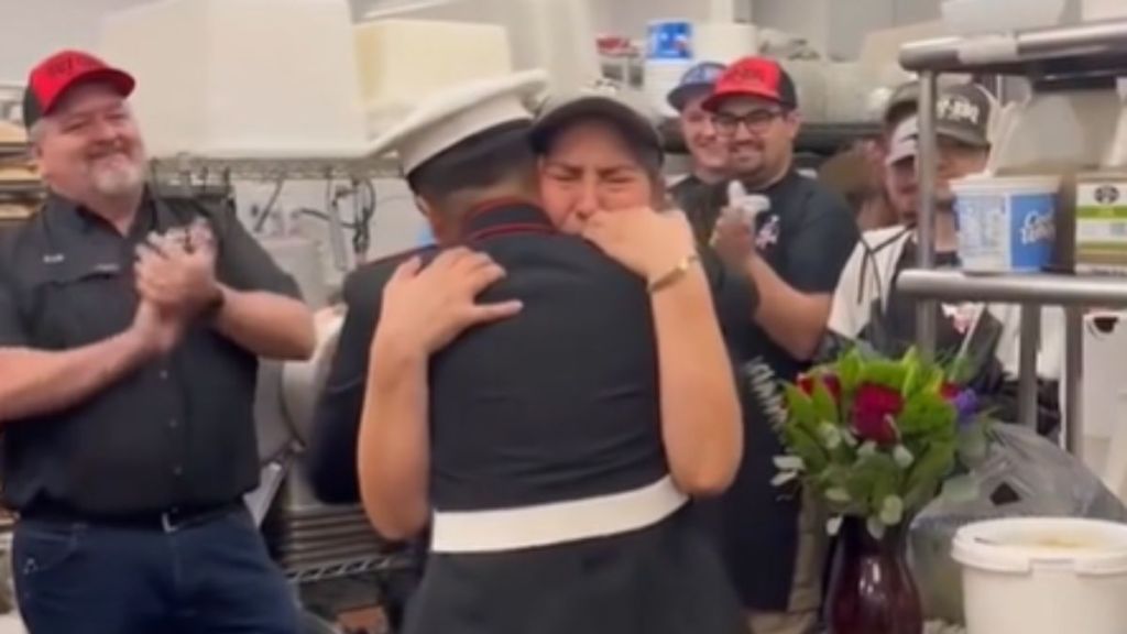 A mom hugs her Marine daughter while others applaud.