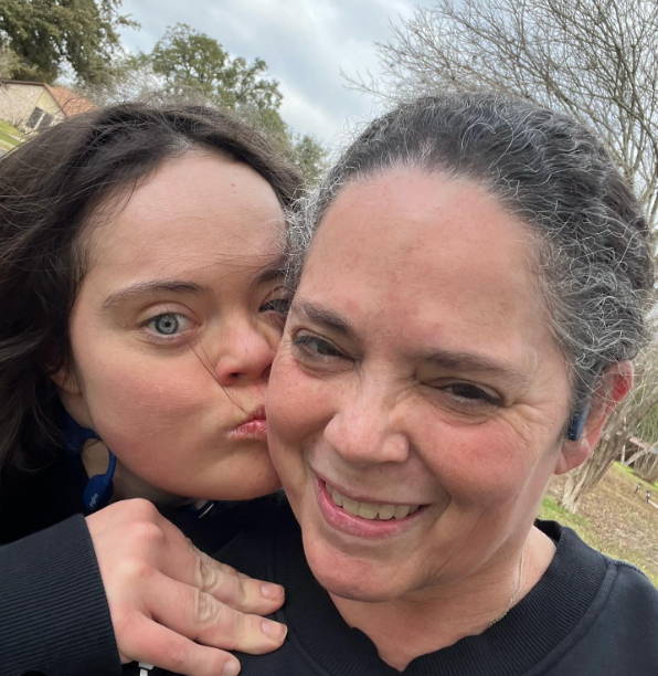Sandy Williamson smiles as she takes a selfie outside with her daughter, Kayleigh, who is kissing her mom on the cheek as she looks at the camera.