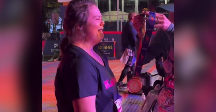 Kayleigh Williamson cries after crossing the finish line at the NYC Marathon. Someone holds out a medal for her.