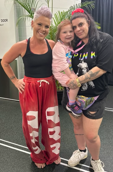 Pink, Lillian, and Angela smile for a photo together. Lillian is in Angela's arms but she's next to Pink.