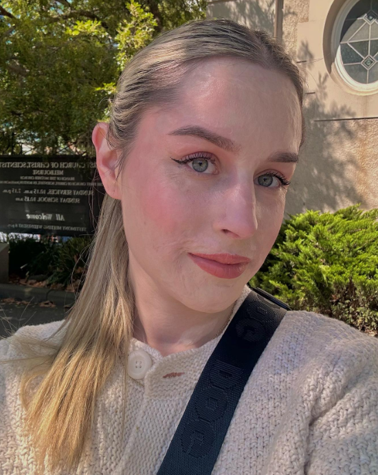 Stephanie Coral Browitt smiles softly for a selfie outside.