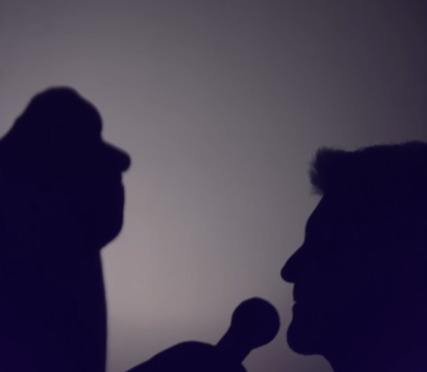 View of Shadow Ace's performance on "AGT." His shadow puppet is holding a mic up to the shadow of Simon Cowell.