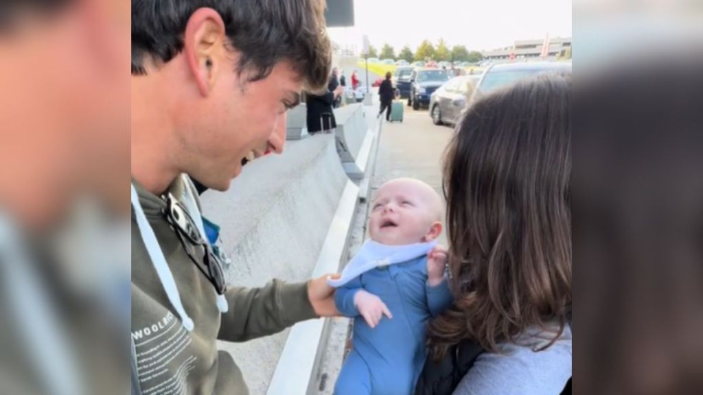 A man smiles while meeting the little baby in a woman's arms.