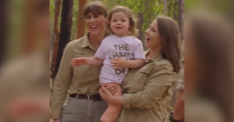 Terri smiles as she stands next to Bindi Irwin who is holding her daughter Grace (Steve Irwin's granddaughter) in her arms. They're happily walking outdoors.