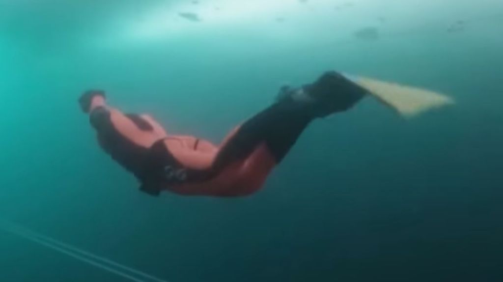 A swimmer with a monofin diving deep under the ice.