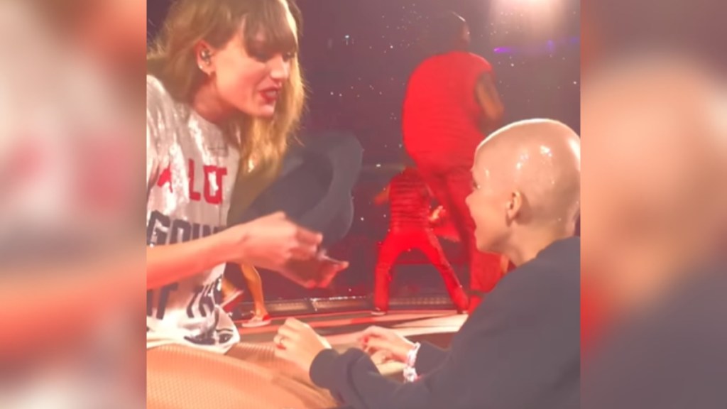 Taylor Swift smiles as she sits on the Eras Tour stage. She's handing her hat to 9-year-old Scarlett Oliver.