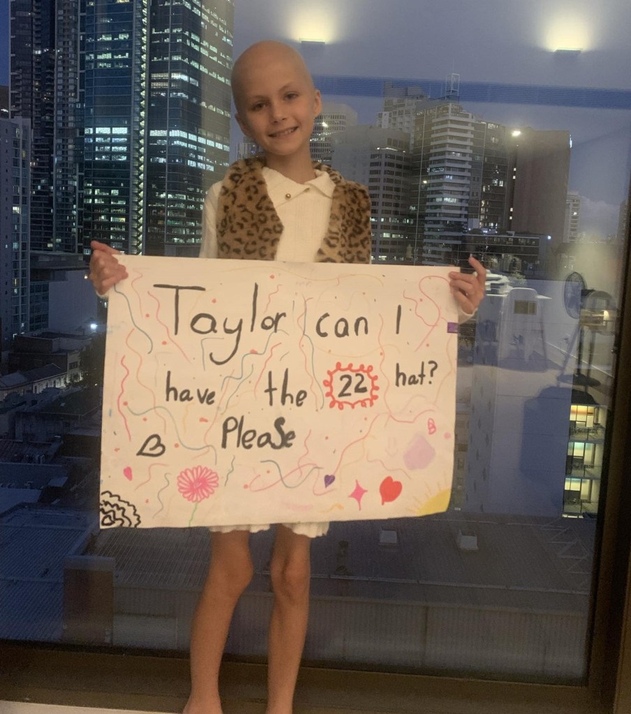Nine-year-old Scarlett Oliver smiles as she holds a sign that reads: Taylor can I have the 22 hat? Please