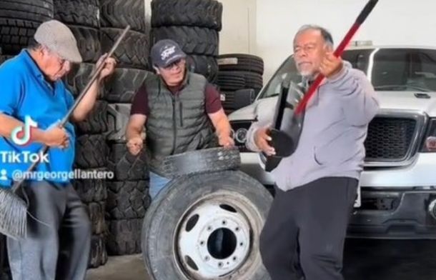 Men playing broom "guitars' and tire "drums" in an auto shop.