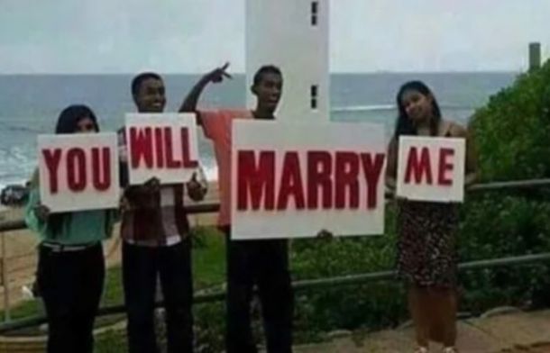 A marriage proposal gone wrong. Four people have word plaques that are supposed to say "Will you marry me," but they are standing in the wrong order so it says "You will marry me."