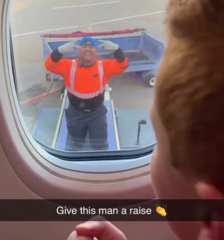 An airline worker plays a game with a kid through the window of an airplane.