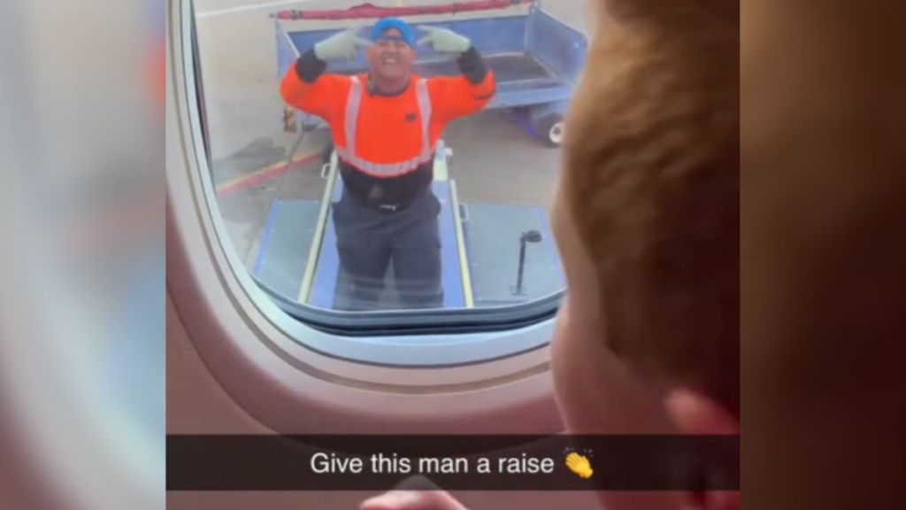 An airline worker plays a game with a kid through the window of an airplane.