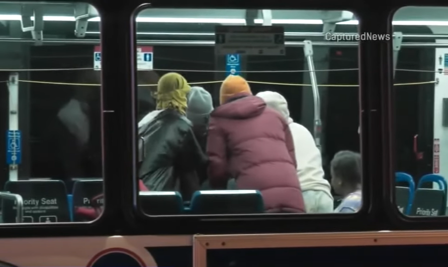 View from the outside of a Chicago bus. A group of people are huddled together, standing and talking, inside.