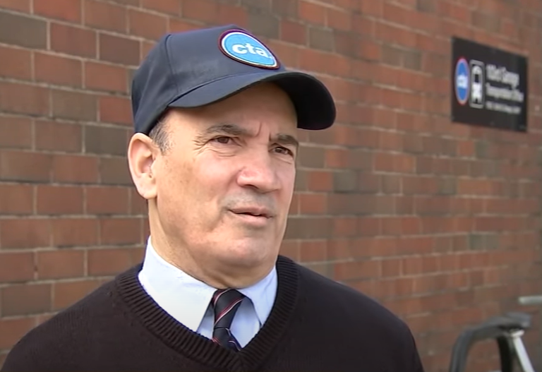 Bus driver Anastasios Adamopoulos stands outside, wearing a CTA hat, as he talks with local news.