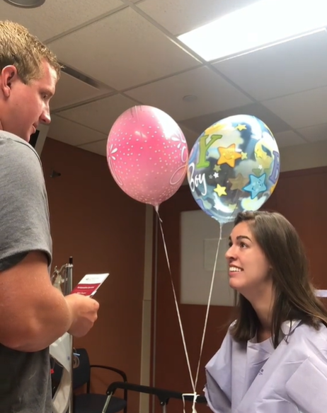 A surgery patient in a hospital gown is thrilled to announce to her husband that she's pregnant.