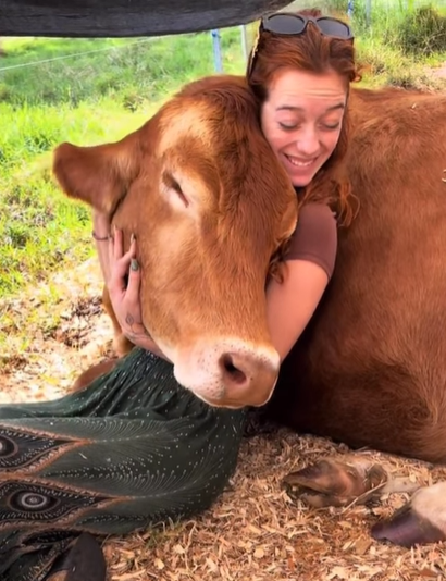 A woman smiles as she cuddles with a cow.