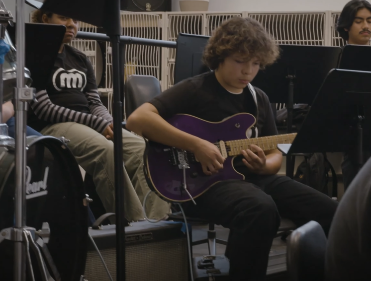 A student sits as he plays a guitar.
