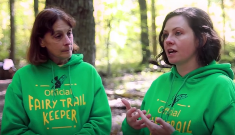 Two women in matching green hoodies standing in the forest.