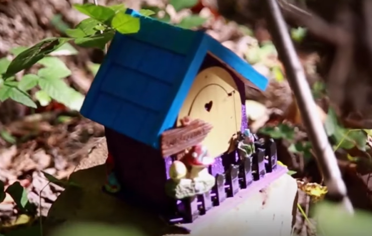 A tiny fairy house with a blue roof in the woods.